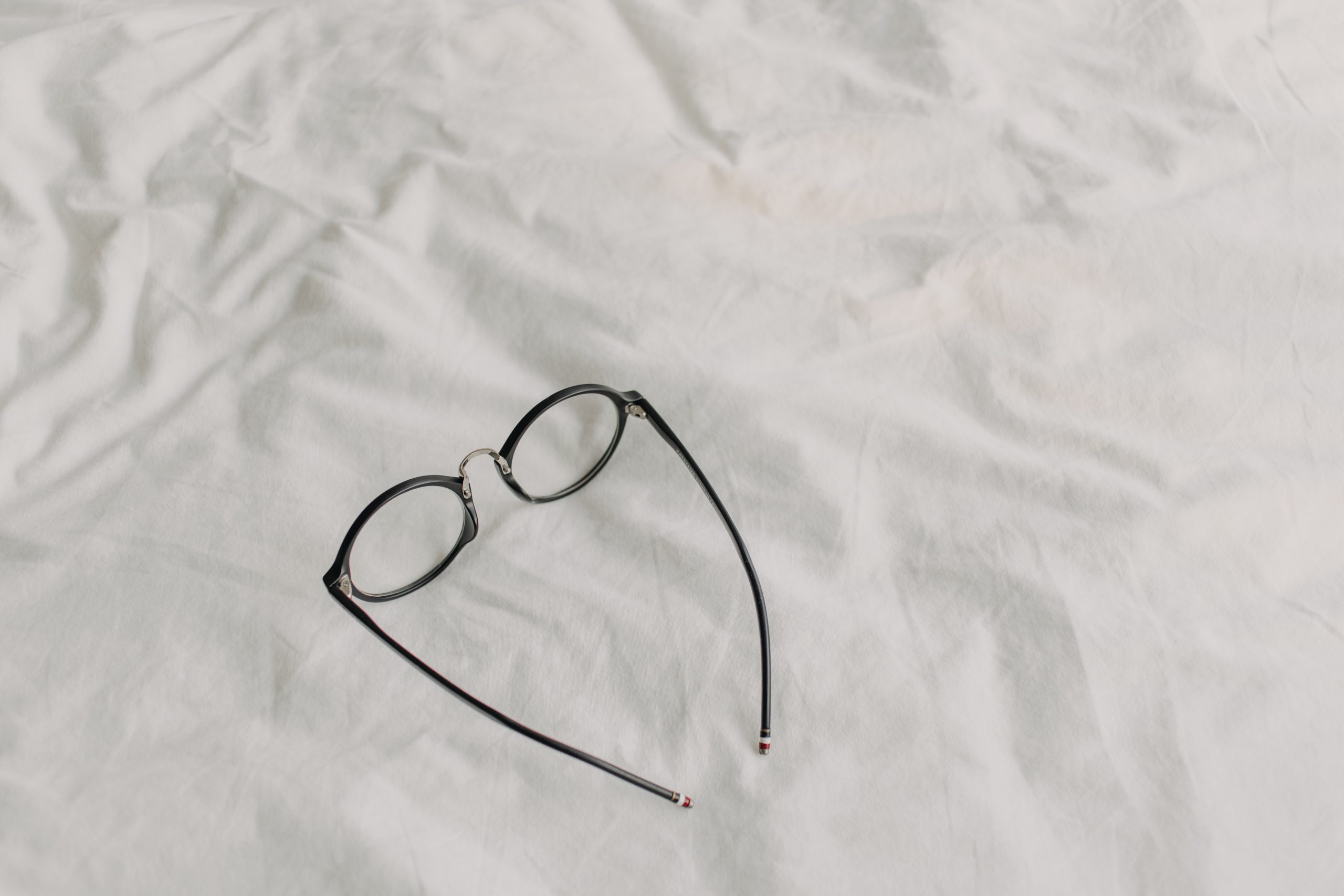 Eyeglasses with black plastic temple on white bed sheet. Concept of read and relax.